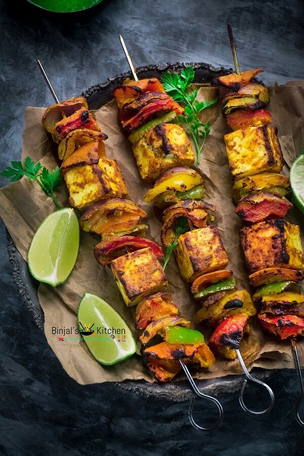 Grilled vegetable and paneer skewers with lime wedges.